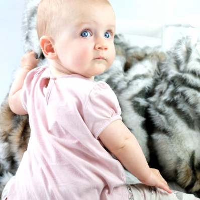 photo shoot of a cute baby with big blue eyes crawling on a fur rug